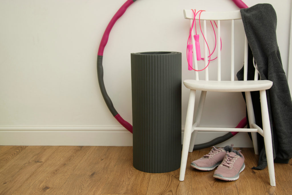 Fitness equipment including runners, hula hoop and skipping rope resting against a white wooden chair and wall.